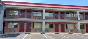 Een motel met twee verdiepingen, rode deuren en ramen, een rood dak en een parkeerplaats met aangewezen parkeerplaatsen voor mindervaliden.