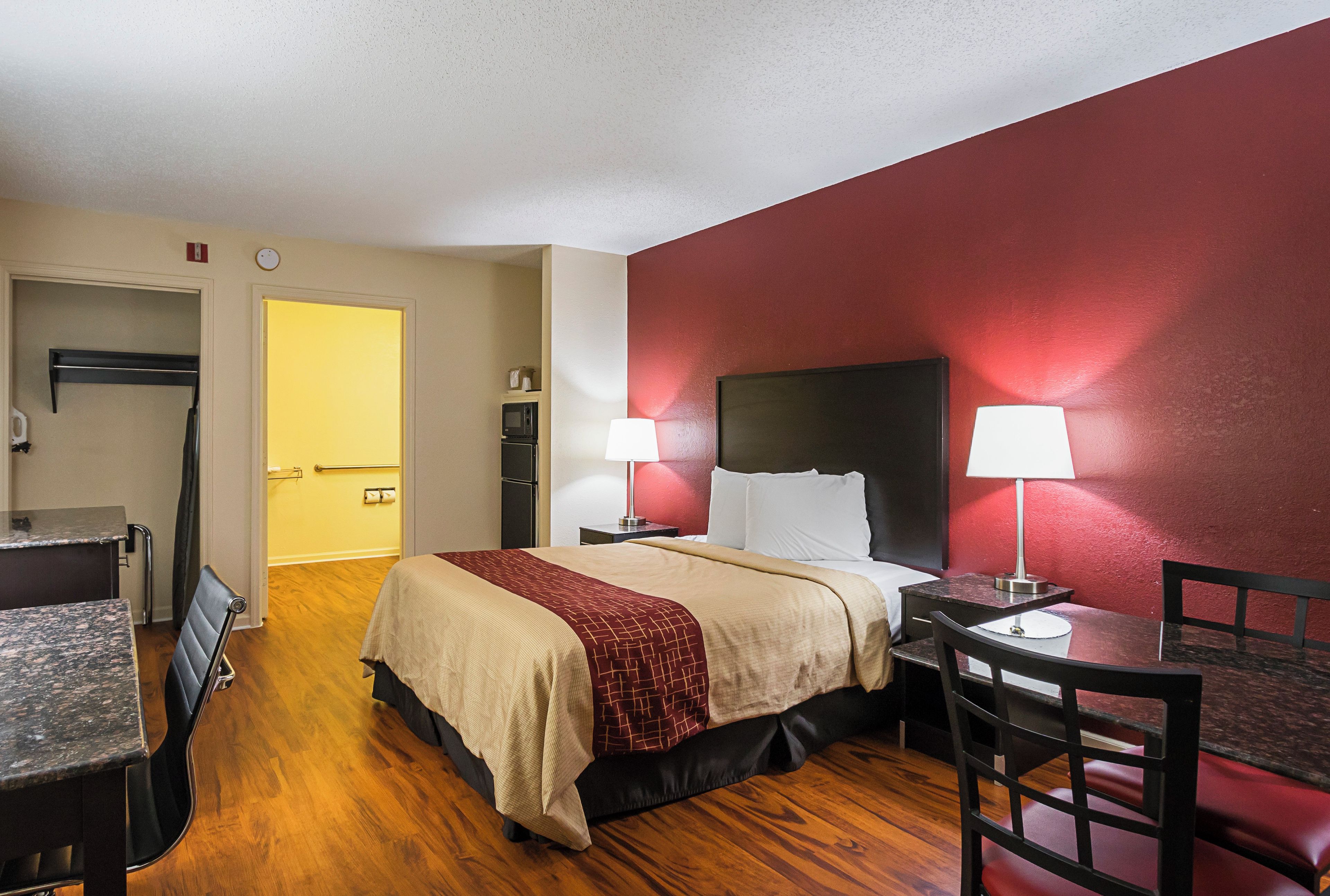 A hotel room with a bed, bedside tables, a desk, a chair, and a microwave.