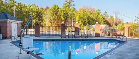 A rectangular swimming pool with a diving board, surrounded by a brick wall and a metal fence.