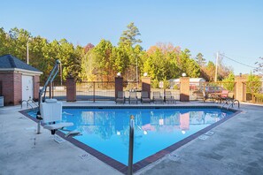 Una piscina rectangular con tabla de salto, rodeada por un muro de ladrillo y una valla metálica.