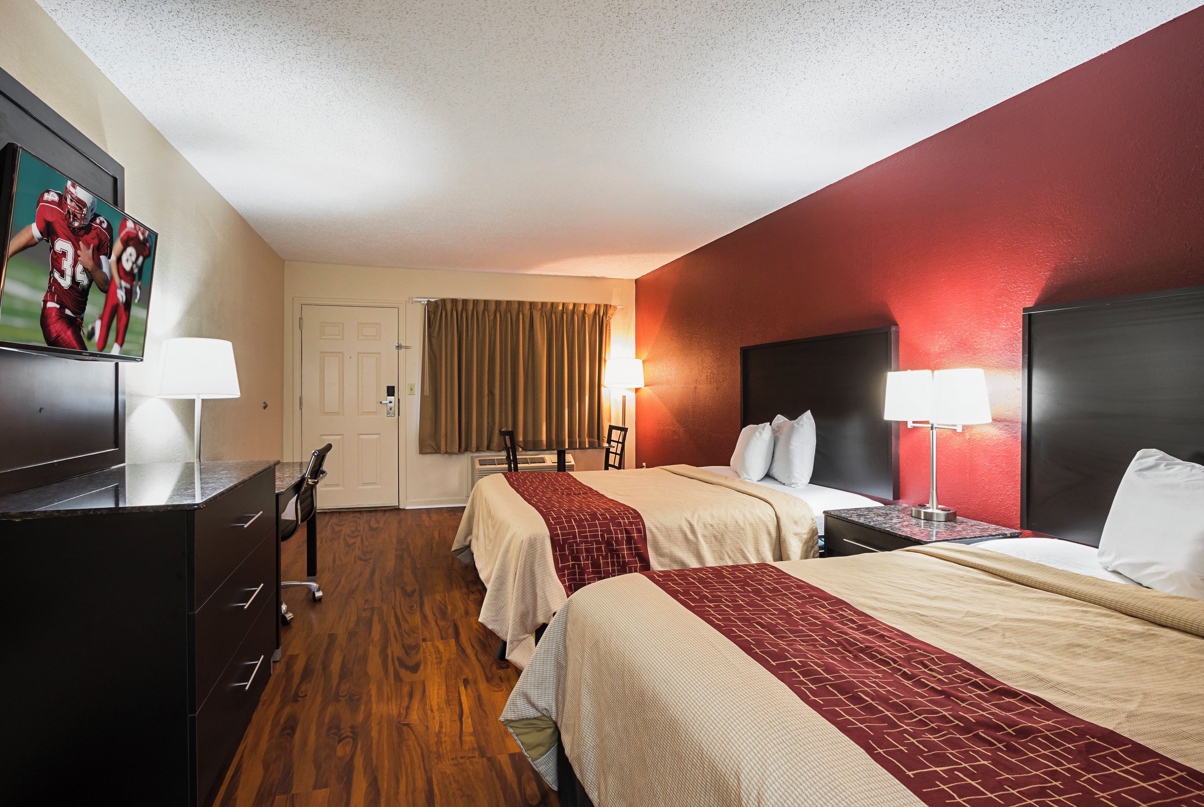 A hotel room with two beds, a desk, a television, and a window with curtains.
