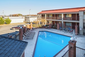 A hotel with a swimming pool, outdoor seating, and a parking lot.