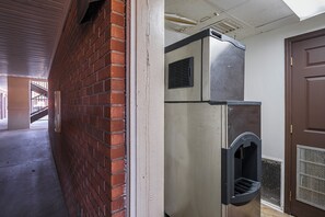 Un pasillo con pared de ladrillo, una puerta y un refrigerador de acero inoxidable.