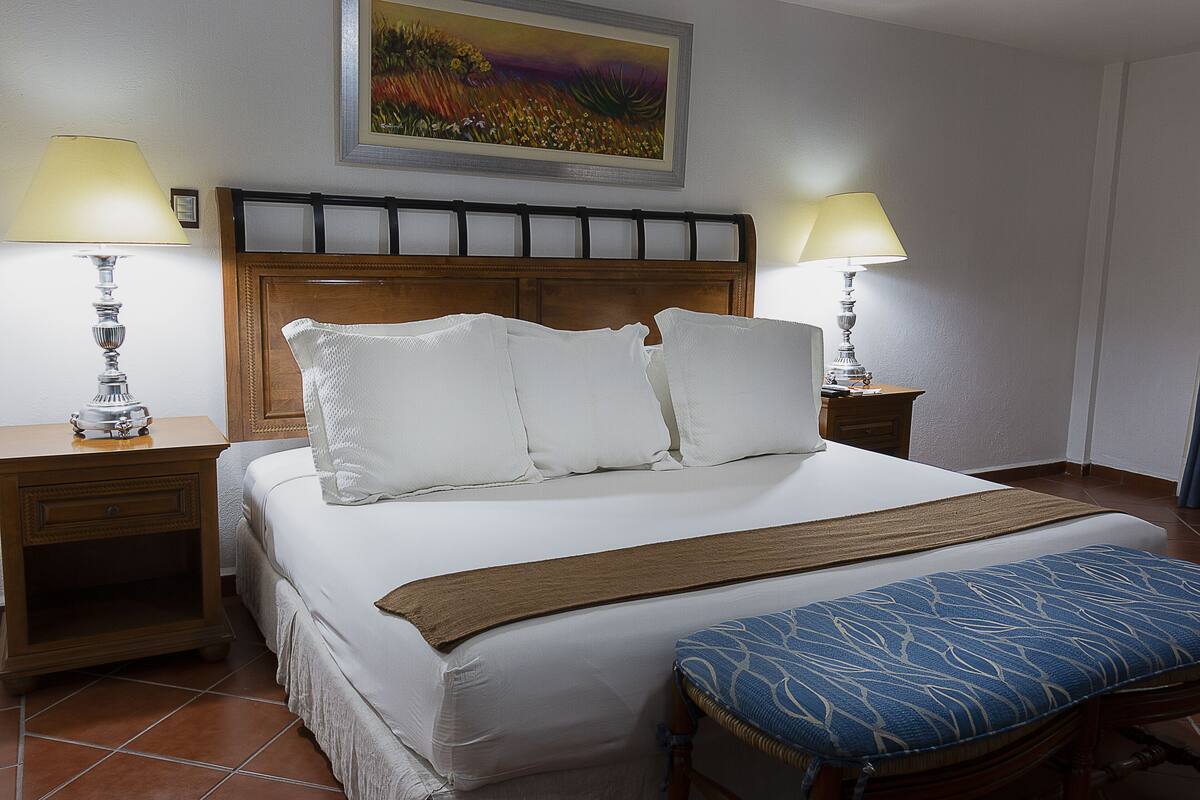 A neatly made bed with white linens, a wooden headboard, and two bedside lamps.