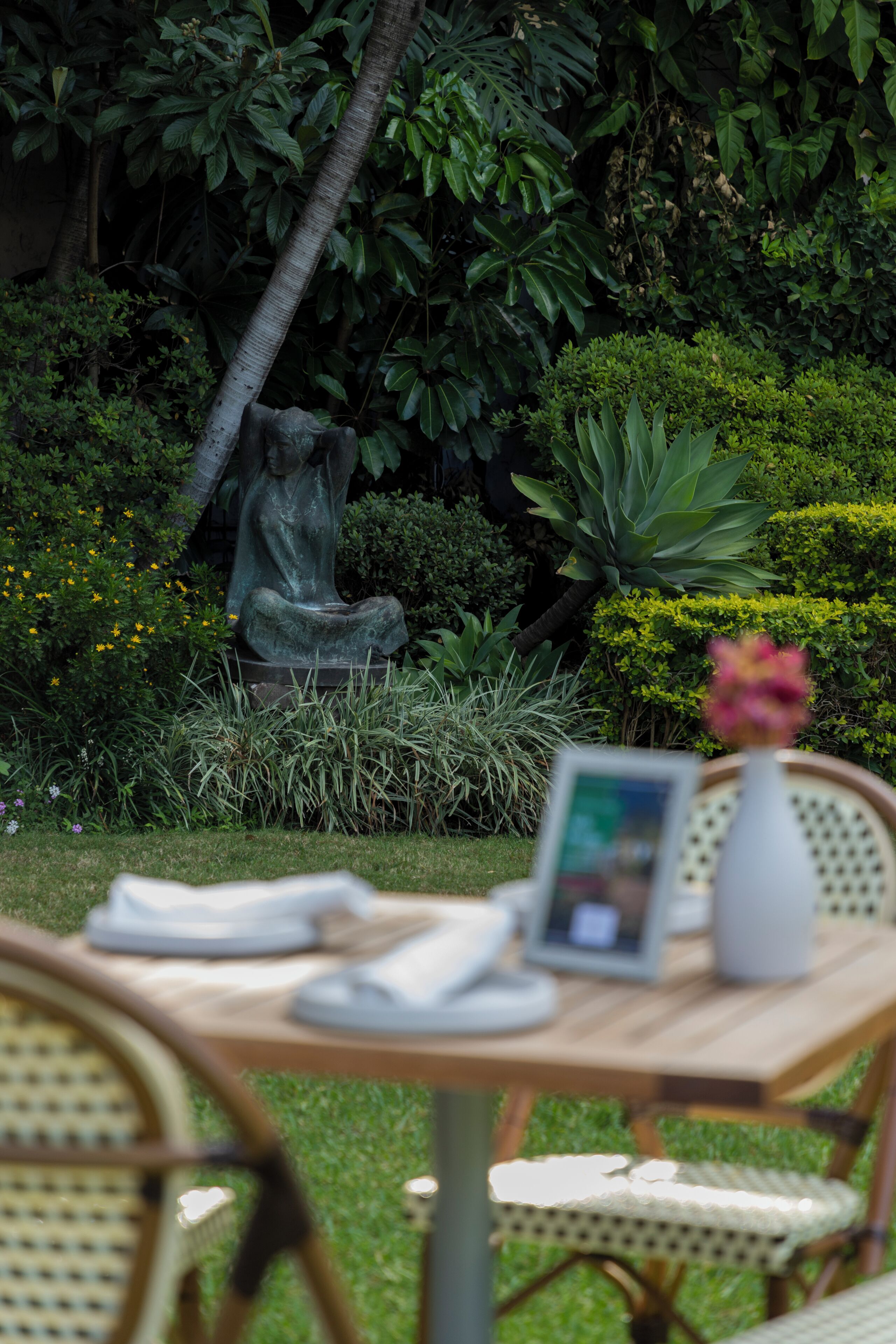 A garden with a statue, a table with chairs, and a vase with flowers.