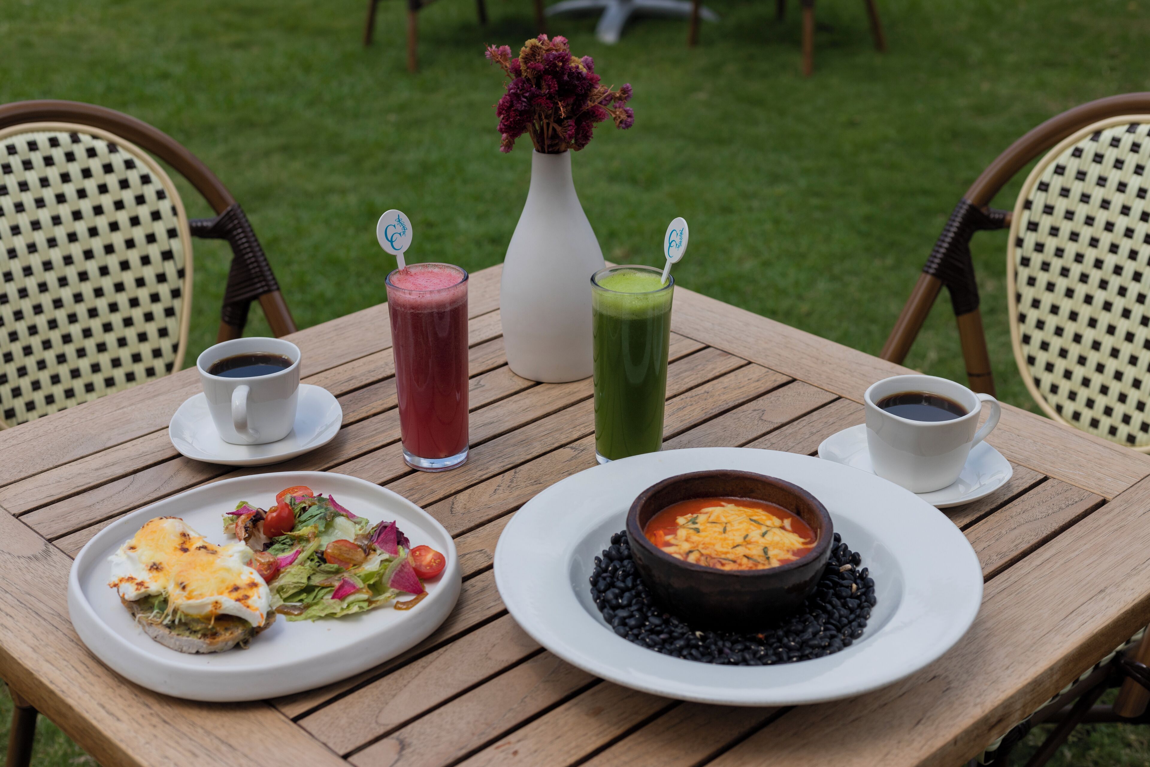 A wooden table with a white plate of food, a bowl of soup, and two drinks.