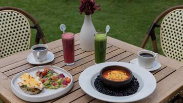 A wooden table with a white plate of food, a bowl of soup, and two drinks.