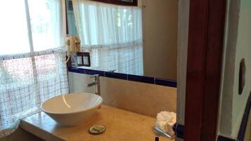 Un baño con un lavamanos grande blanco, un espejo y una ventana con cortinas blancas.