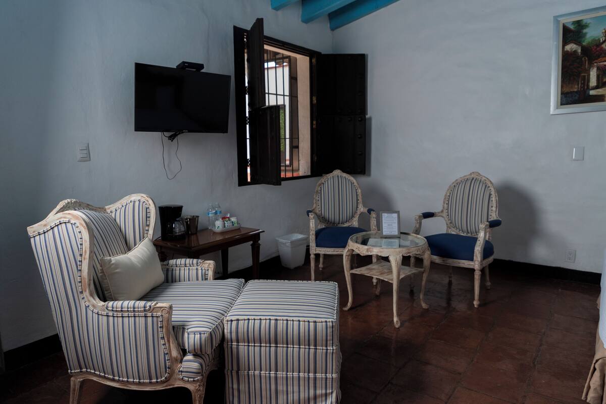 A room with striped upholstered furniture, a television mounted on the wall, and a window with open shutters.