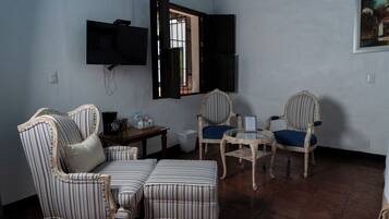 A room with striped upholstered furniture, a television mounted on the wall, and a window with open shutters.