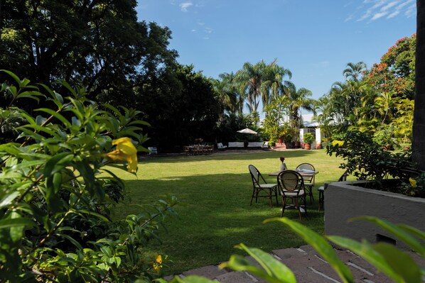 Un jardín cuidado con césped, zona de estar exterior y diversas plantas y árboles.