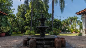 A stone fountain with water spouting from the top, surrounded by potted plants and palm trees in a garden setting. - Hotel Boutique Casa de Campo (Cuernavaca)