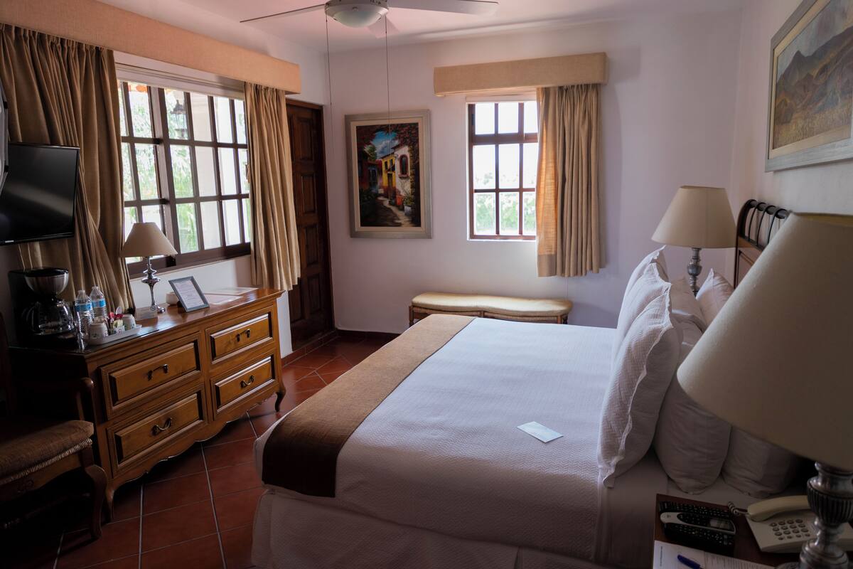 A hotel room with a large bed, a desk with a lamp, a television, and a painting on the wall.