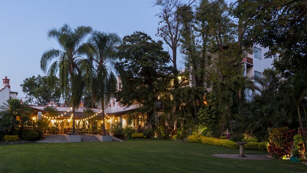 A large, white building with a red roof, surrounded by lush greenery and palm trees. - Hotel Boutique Casa de Campo (Cuernavaca)