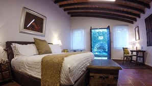 A bedroom with a large bed, a wooden chest, a nightstand, a lamp, and a framed picture on the wall. - Hotel Boutique Casa de Campo (Cuernavaca)
