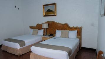 A hotel room with two single beds, a wooden headboard, a nightstand with a lamp, and a framed picture on the wall.