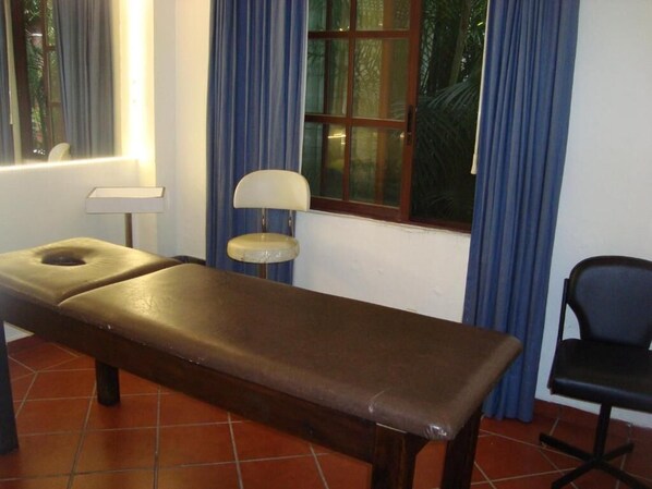 A room with a massage table, a chair, a lamp, and a window with curtains. - Hotel Boutique Casa de Campo (Cuernavaca)