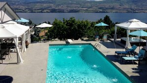 A pool with a view of mountains and a lake. There are lounge chairs and umbrellas around the pool. - Le Chateau du Lac (West Kelowna)