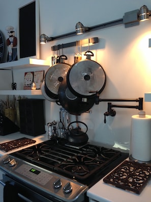 Una cocina con estufa a gas, hervidor y un colgador para ollas.