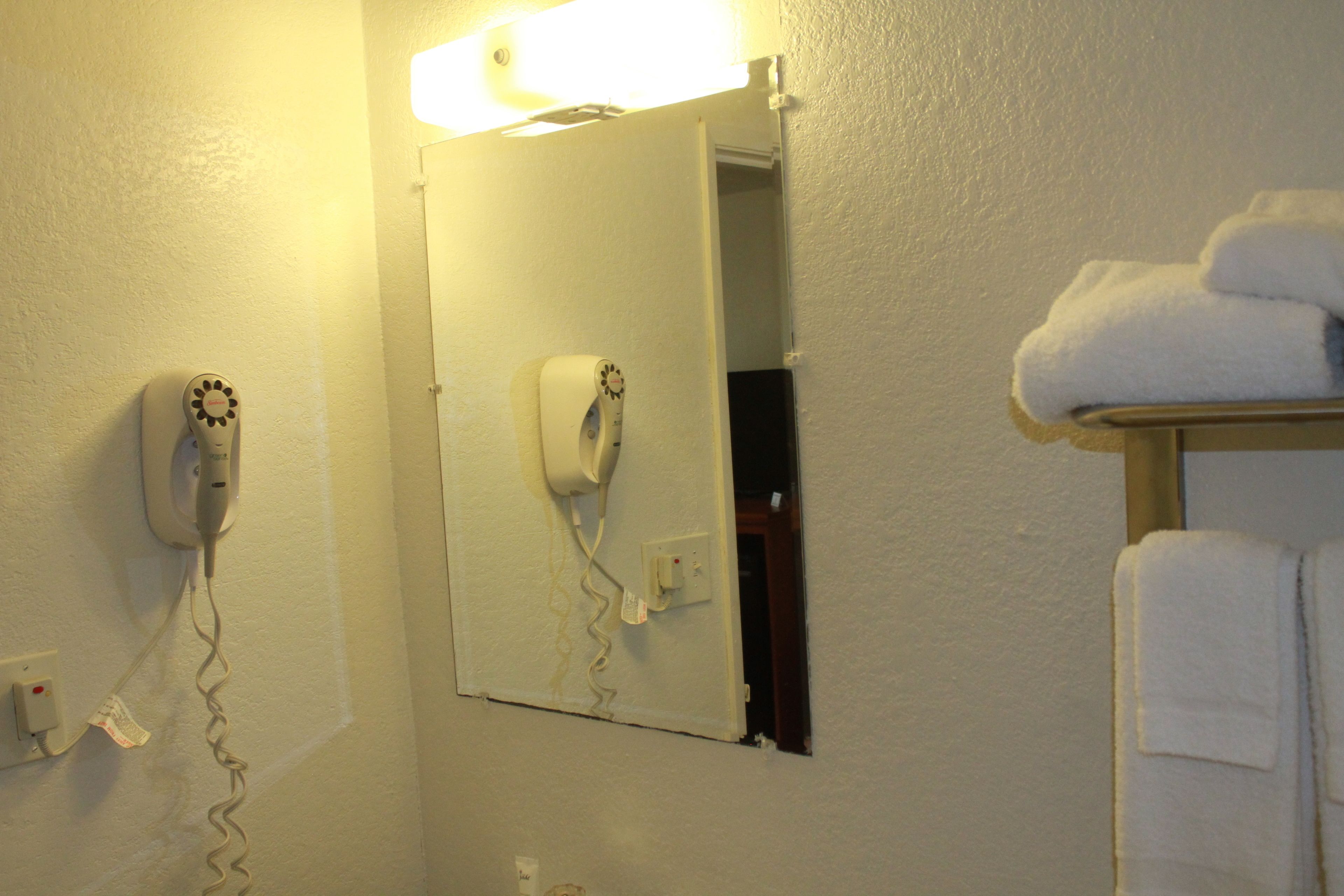 Un baño con secador de pelo montado en la pared, un espejo y un perchero con toallas.