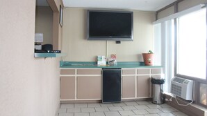 Una kitchenette pequeña con un televisor montado sobre la encimera, un cubo de basura y una planta en el alféizar de la ventana.