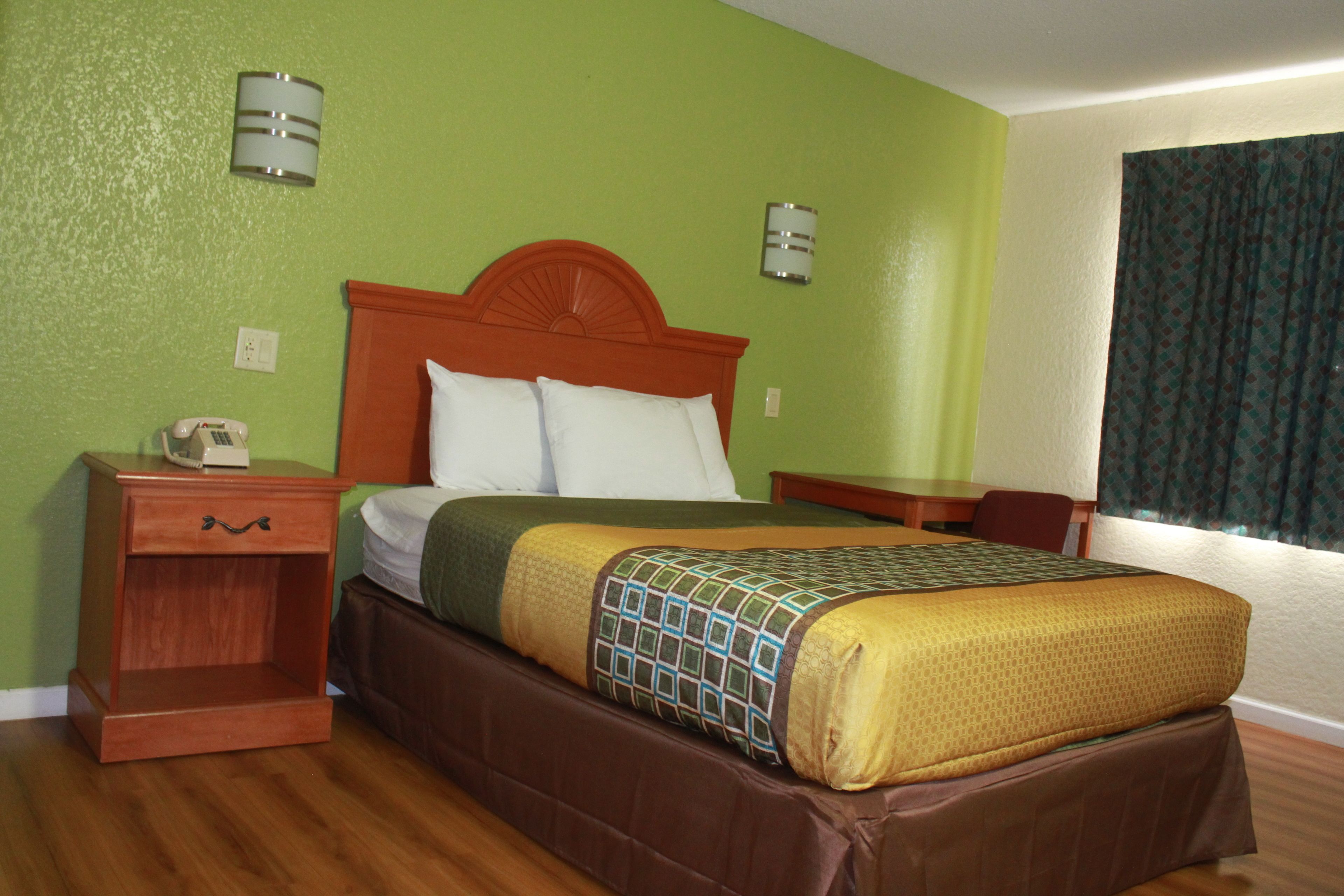 A hotel room with a wooden bed, green walls, and a window with curtains.