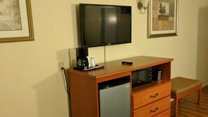 Habitación de hotel compacta con un armario de madera, un televisor de pantalla plana, una cafetera y un refrigerador pequeño.