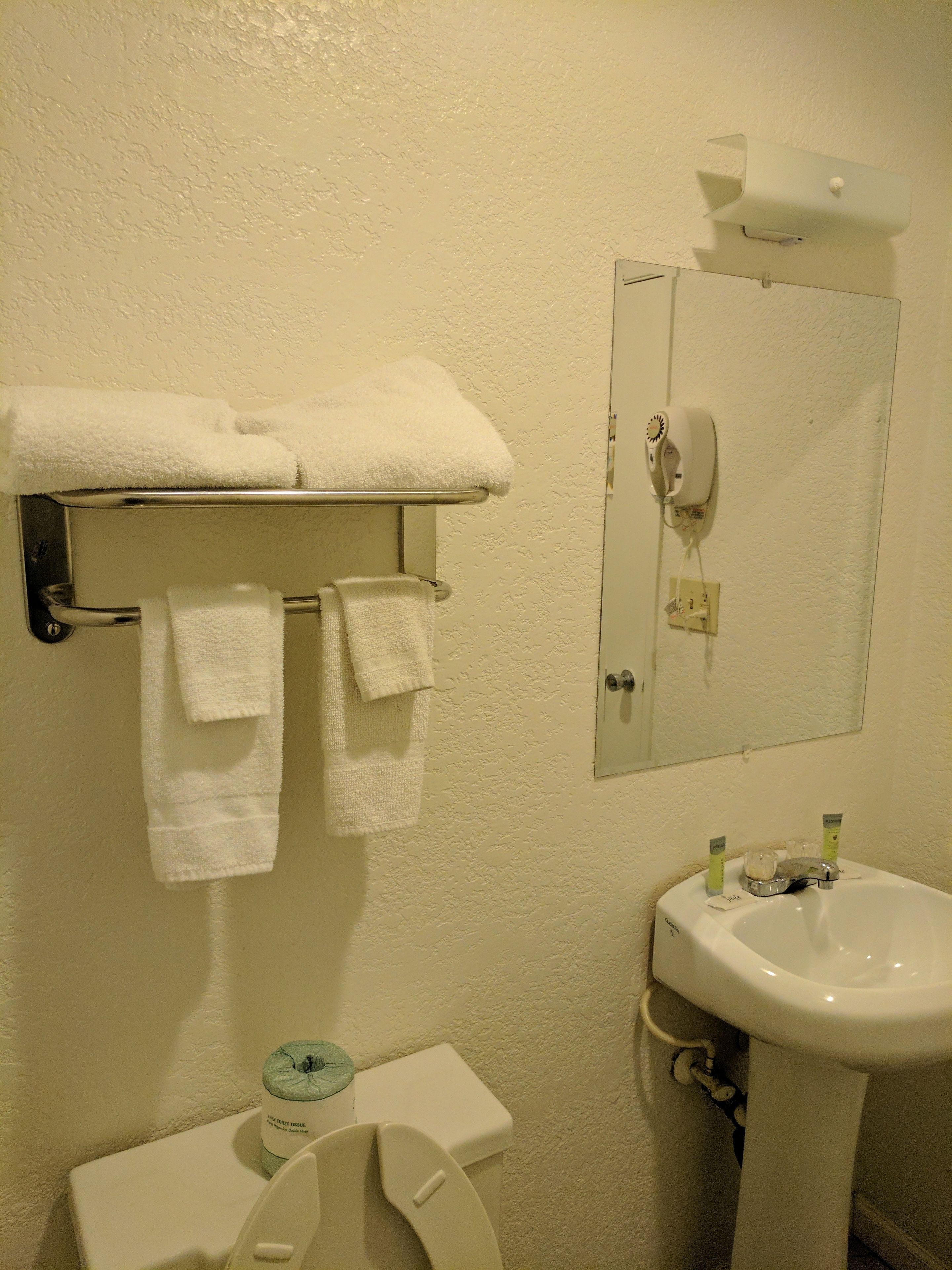 A bathroom with a toilet, sink, towel rack, and a mirror.