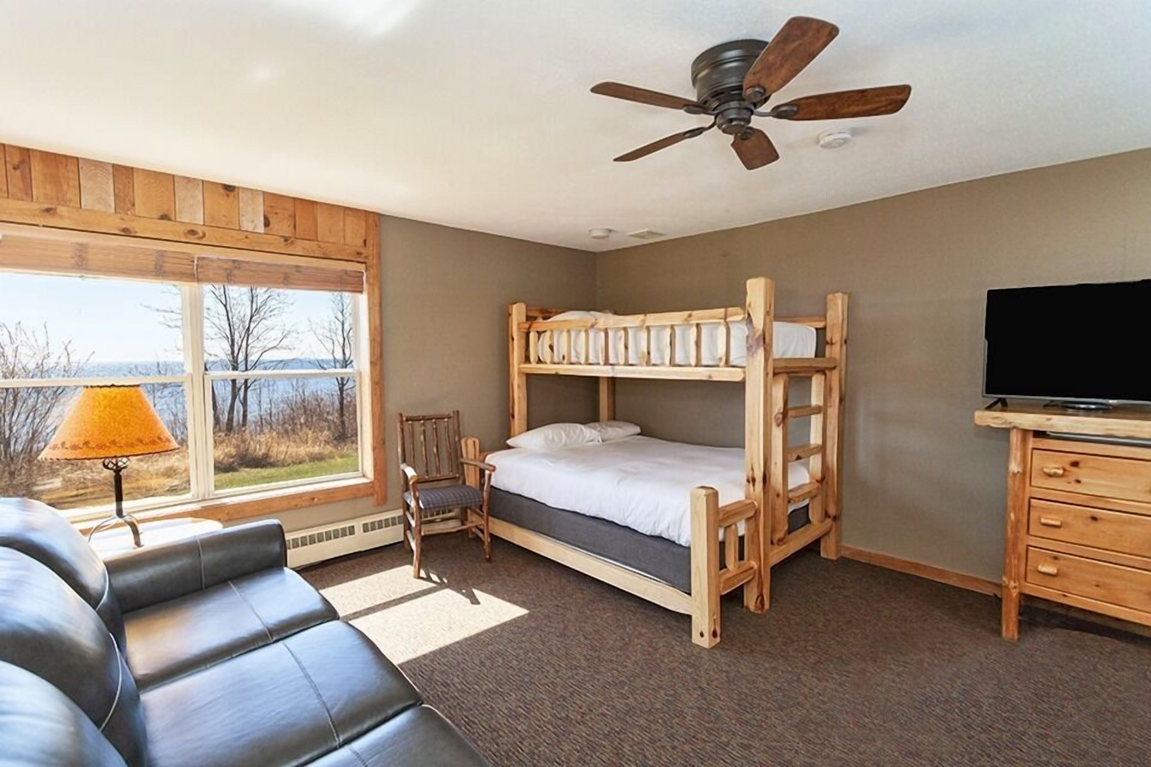 A bunk bed room with a ceiling fan, a TV, a window with a view, a chair, and a sofa.