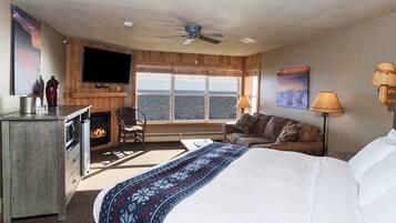 A hotel room with a bed, a TV, a fireplace, a sofa, and a view of the sea.