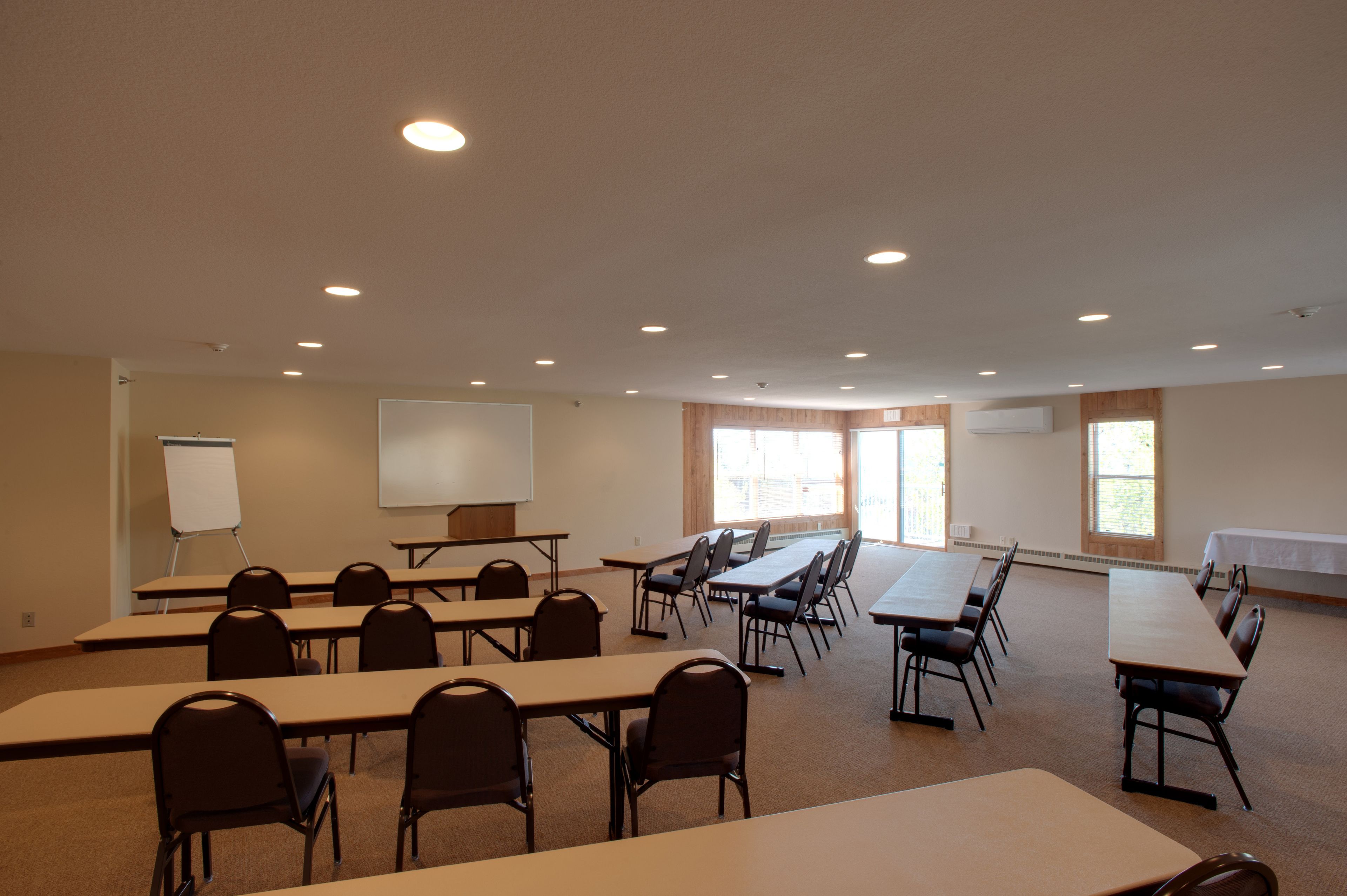 A conference room with multiple tables and chairs, a whiteboard, and a projector screen.