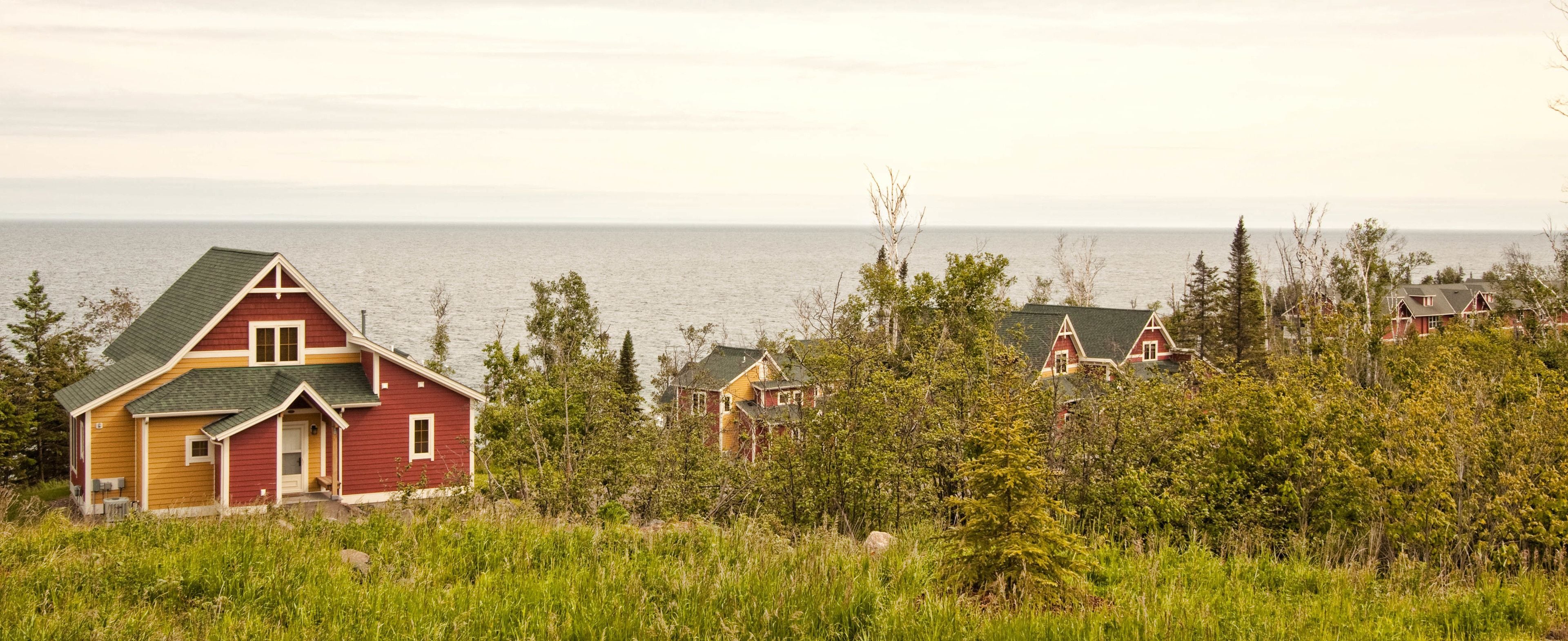 A coastal house with a red and yellow exterior, surrounded by greenery and overlooking the sea.