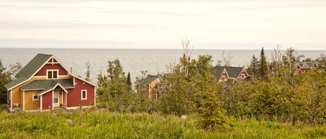 A coastal house with a red and yellow exterior, surrounded by greenery and overlooking the sea.
