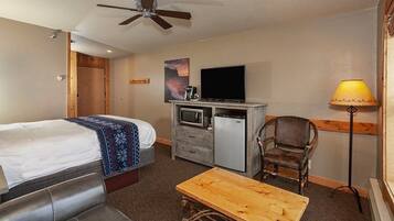 A hotel room with a bed, a desk, a chair, a television, a microwave, and a ceiling fan.