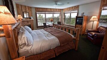 A cozy hotel room with a large bed, wooden headboard, a television, a fireplace, and a view of the outdoors.