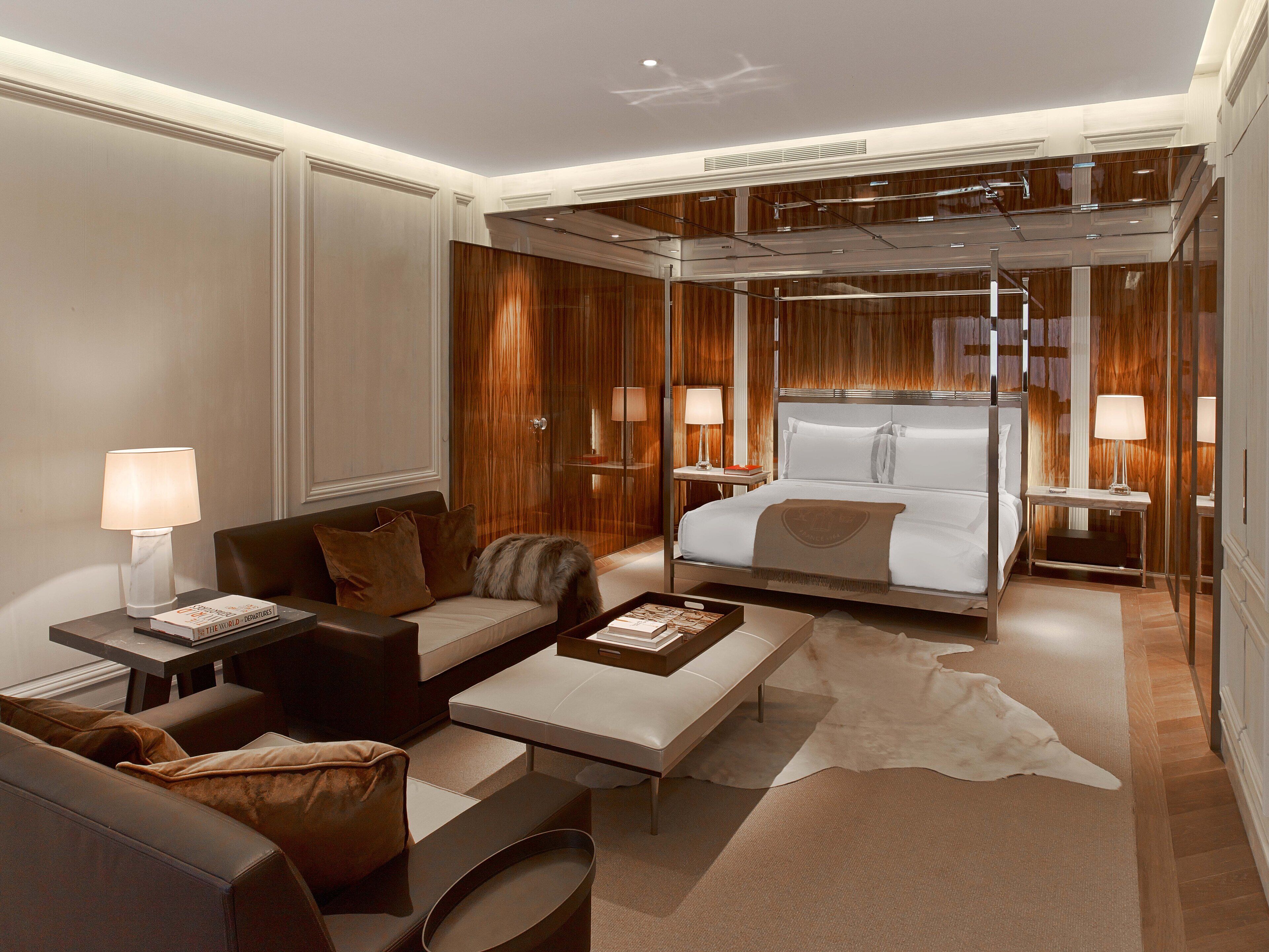 A modern hotel room with a large bed, a sofa, a coffee table, and a desk with a lamp.
