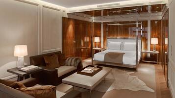 A modern hotel room with a large bed, a sofa, a coffee table, and a desk with a lamp.