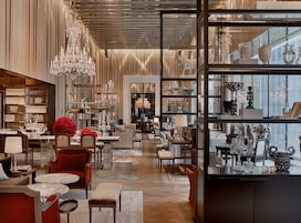 A luxurious hotel lobby with elegant furniture, a grand chandelier, and a display of fine china and glassware.