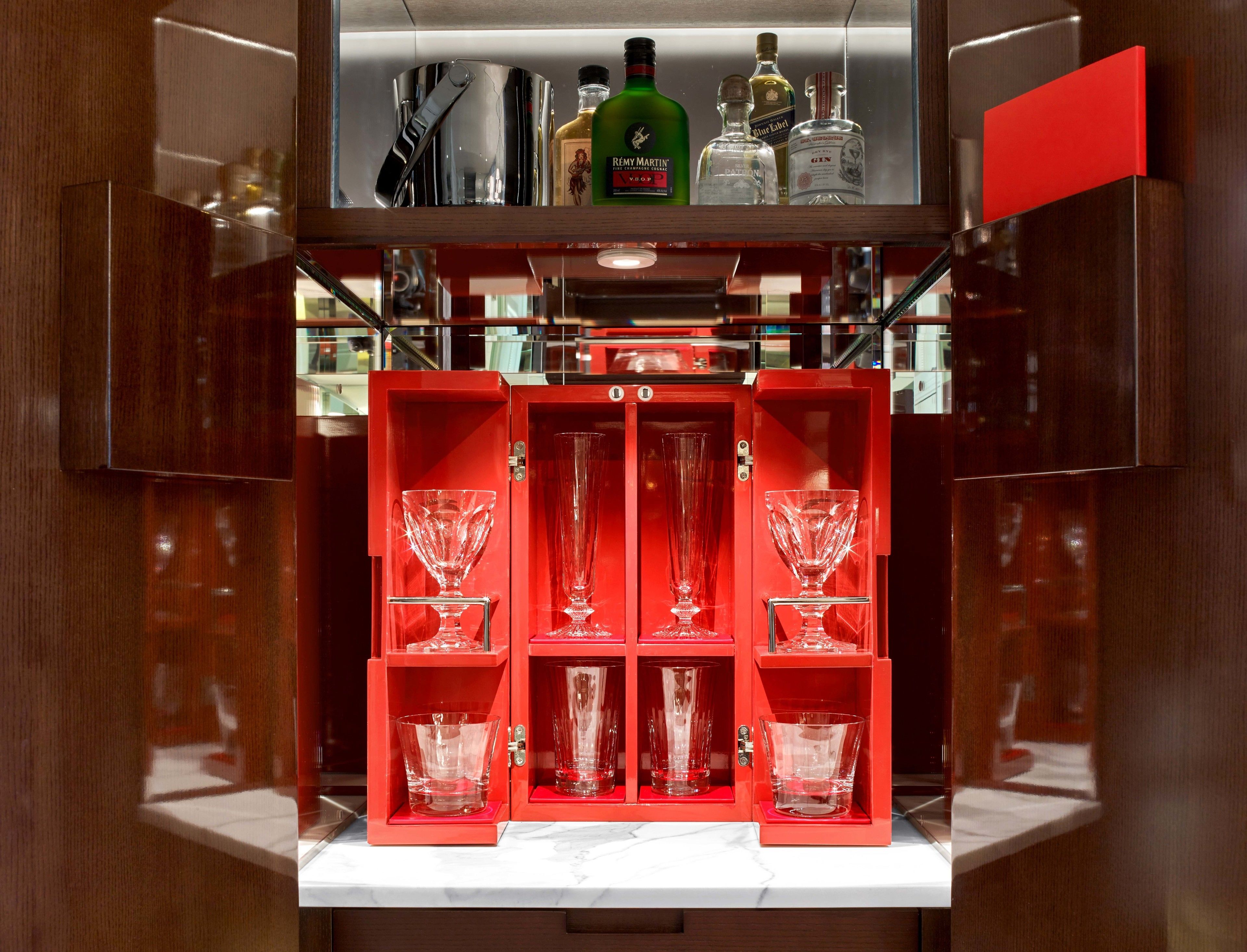 Una zona de bar con un mueble rojo que alberga diferentes copas y botellas.