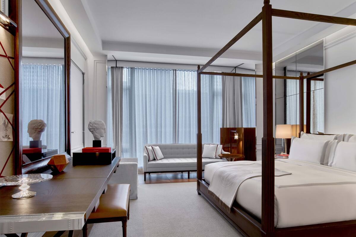 Una cama con dosel de madera, un sofá, un escritorio con un banco y un espejo grande.