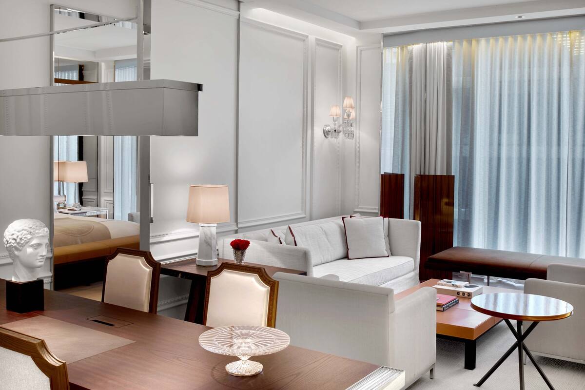 Una habitación de hotel moderna con zona de comedor, un sofá, una mesa y un pastel decorativo.