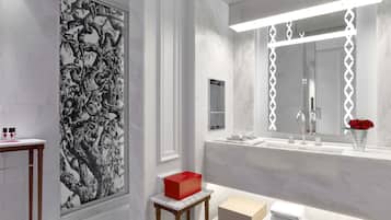 Uma casa de banho moderna com um espelho grande, paredes de mármore branco, um mural decorativo a preto e branco e uma pequena mesa com artigos de higiene pessoal.