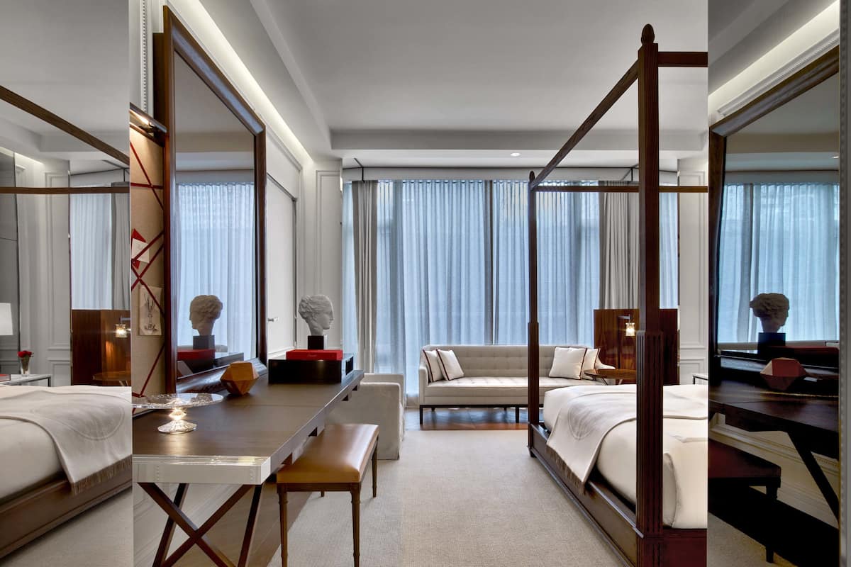 Habitación de hotel con cama con dosel, sofá, escritorio con silla y un espejo grande.