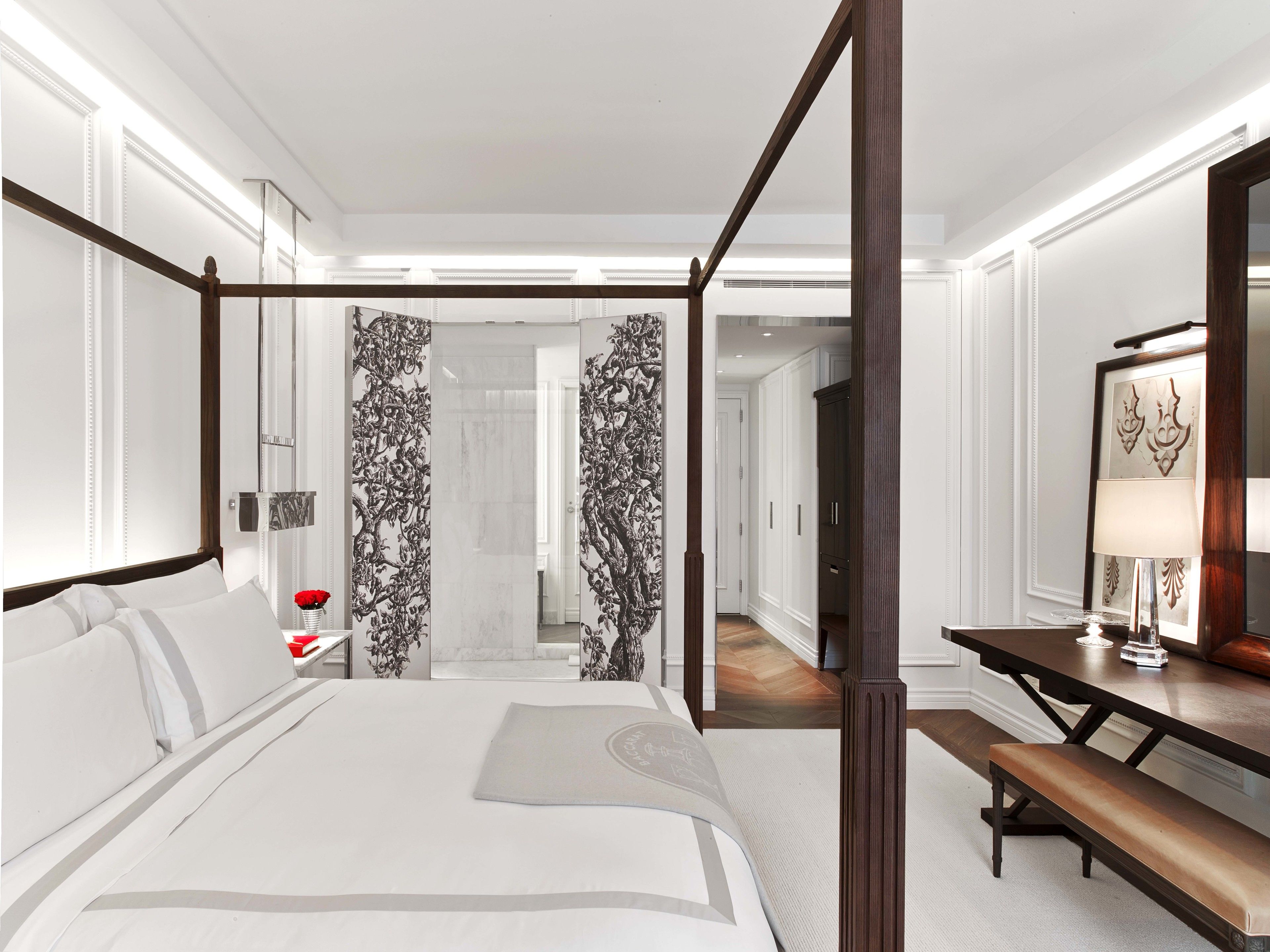 A modern hotel room with a four-poster bed, a wooden desk, and a large mirror.