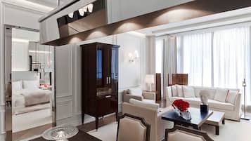 A modern hotel room with a dining area, a large dark wooden cabinet, a white sofa, and a dining table with a vase of red roses.