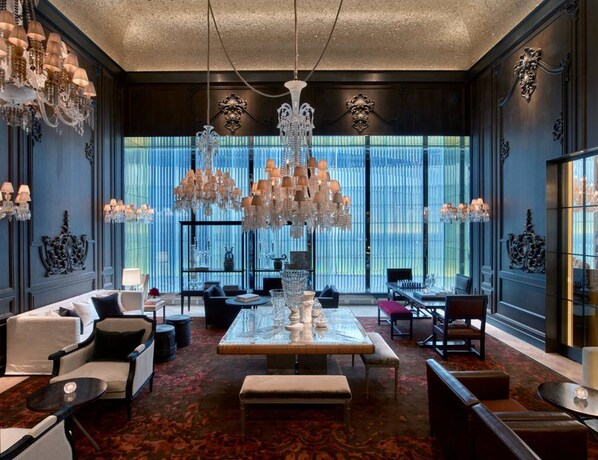 A luxurious hotel lobby with a grand chandelier, elegant furniture, and large windows with blue curtains. - Baccarat Hotel and Residences New York (New York)