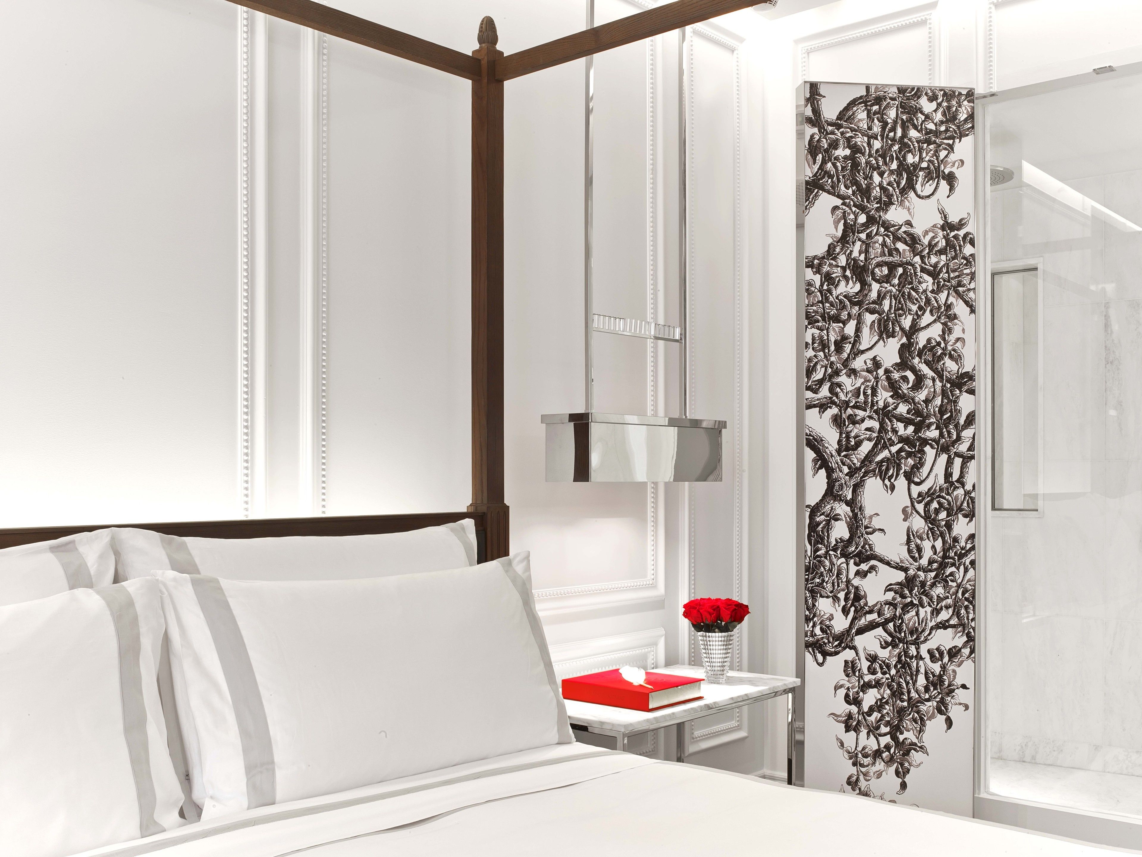 A hotel room with a four-poster bed, a bedside table with a vase of red roses, and a decorative wall panel.