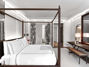 A four-poster bed with a bench, a desk with a lamp, and a mirror in a hotel room.