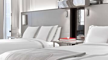 A modern hotel room with two beds, a small table, and a red book on the nightstand.