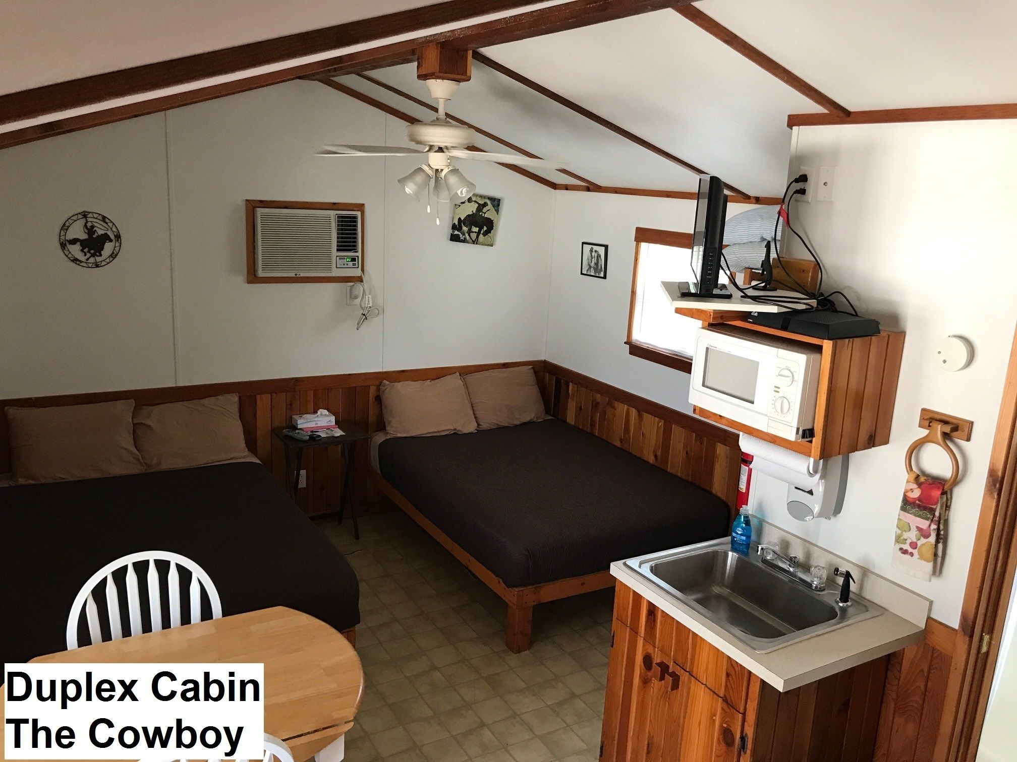 A duplex cabin with a kitchenette, two beds, a ceiling fan, and a mounted TV.